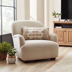 a living room with a chair, television and potted plants on the hardwood floor