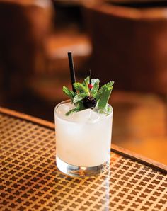 a glass filled with ice and topped with a green leafy garnish sitting on top of a wooden table