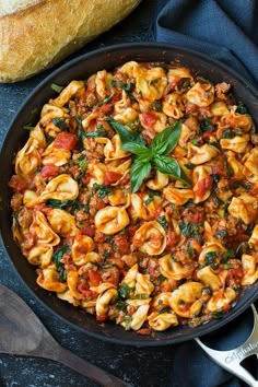 a skillet filled with pasta and spinach on top of a blue table cloth