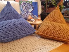 two crocheted pillows sitting on top of a wooden floor next to a table