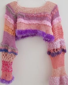 a knitted sweater with purple, pink and orange stripes on the sleeves is hanging from a hook