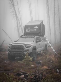 the truck is parked in the foggy forest with its roof up and it's lights on