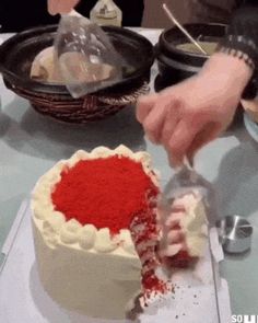 a person is cutting into a cake with red frosting on the top and white icing on the bottom