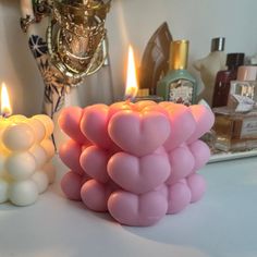 two candles that are sitting next to each other on a table with perfume bottles in the background