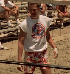 a young man standing in front of a net on top of a sandy beach with people watching