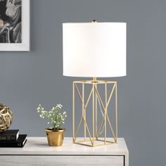 a white lamp sitting on top of a wooden table next to a book and potted plant