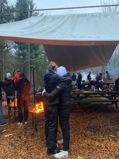 two people hugging each other in front of a tent with food cooking on the fire