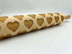 a wooden rolling pin with hearts cut out on the side and a silver object in the background