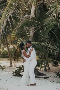 a bride and groom standing in the sand under palm trees