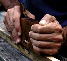 an old man holding something in his hands on a bench with wood slats around him