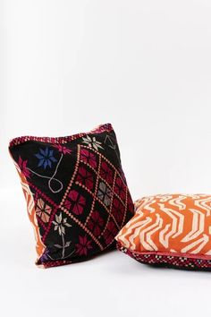 two decorative pillows sitting next to each other on a white surface, one in orange and the other in red