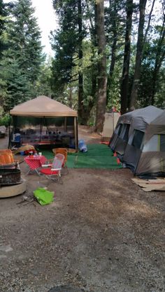 there are many tents in the woods with chairs and tables around them on the ground