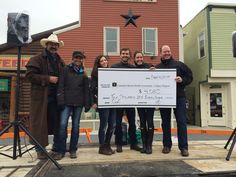 a group of people standing in front of a building holding a large check for $ 1, 500