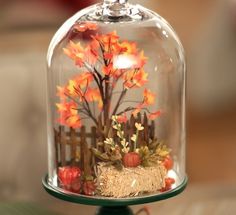 a glass clochel with fake autumn leaves and flowers in it on a table