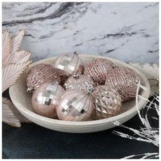 a bowl filled with pink and silver ornaments on top of a marble counter next to leaves