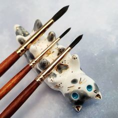 three ceramic cats with paintbrushes in their paws and one has blue eyes on it