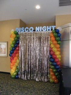 a room filled with balloons and streamers next to a wall that says disco night