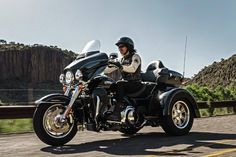 a man riding on the back of a black motorcycle down a road next to mountains