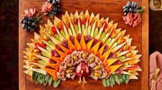 an elaborately designed fruit and vegetable dish on a wooden board with utensils