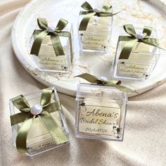 four clear square boxes with green ribbons and bows on them are sitting on a plate