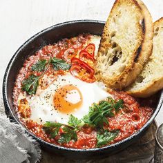 an iron skillet with eggs, bread and tomato sauce