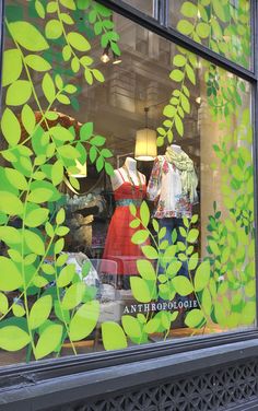 an image of a store window with green leaves on the front and side windows, showing mannequins dressed in dresses