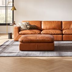 a large brown leather couch sitting on top of a wooden floor next to a window