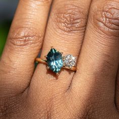 a woman's hand holding a ring with an aqua and white diamond on it