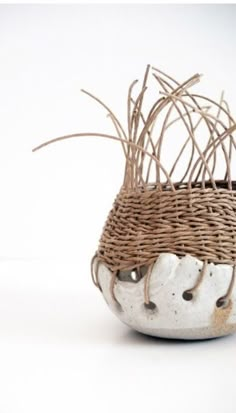 a white and brown vase with some branches in it's basket on a table