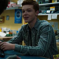 a young man sitting at a table with a computer mouse in his hand and another person standing next to him