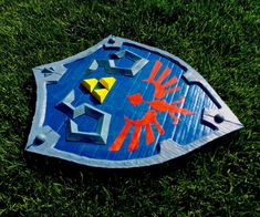 a blue shield with orange and yellow designs on it sitting in the middle of some grass