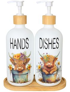 two hand soaps with cows on them are sitting on a wooden tray and one has flowers in it