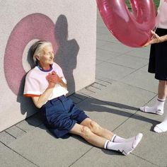 an older man sitting on the ground next to a woman who is holding a balloon