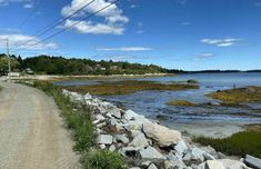 a gravel road next to the ocean with power lines above it