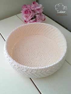 a crocheted bowl sitting on top of a table next to a pink flower