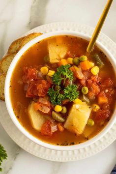 a white bowl filled with vegetable soup on top of a table next to some bread