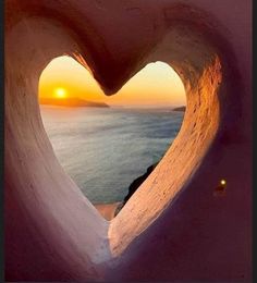 the sun is setting behind a heart - shaped window in an ice cave overlooking the ocean