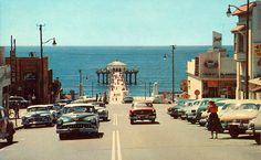 an old photo of cars driving down the road by the ocean with people walking on the sidewalk