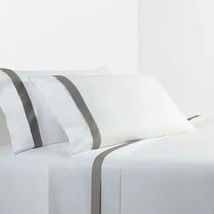 a bed with white sheets and grey striped pillows