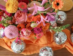 an arrangement of colorful flowers and disco balls on a table with orange napkins in the foreground