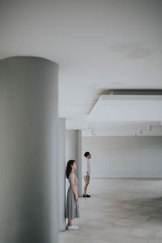 two people standing next to each other in an empty room with white walls and floors