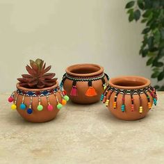 three clay pots with colorful beads and tassels sit on a table next to a potted plant