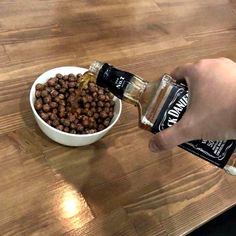 a person pouring something into a white bowl on top of a wooden table next to a dog food dish