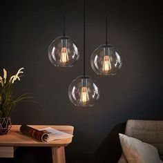 three clear glass globes hang from the ceiling above a table with a book and plant