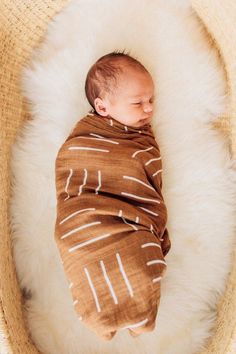 a baby wrapped in a brown blanket laying on top of a white furnishing