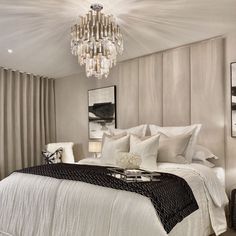 a bedroom with a chandelier hanging from the ceiling and a white bed covered in pillows