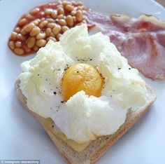 an egg, bacon and baked beans are on a toasted bread with eggs in the middle