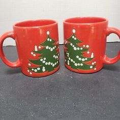 two red coffee mugs with christmas trees painted on them