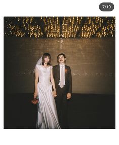 a man and woman standing next to each other in front of a wall with lights