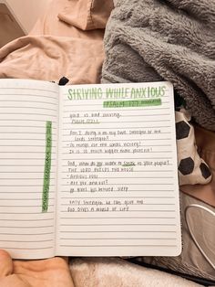 an open notebook sitting on top of a bed next to a pile of blankets and pillows